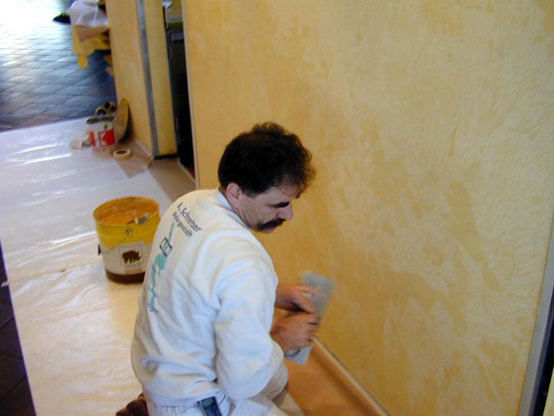 Maler trägt mit dem Spachtel eine gelbe Wandtechnik auf