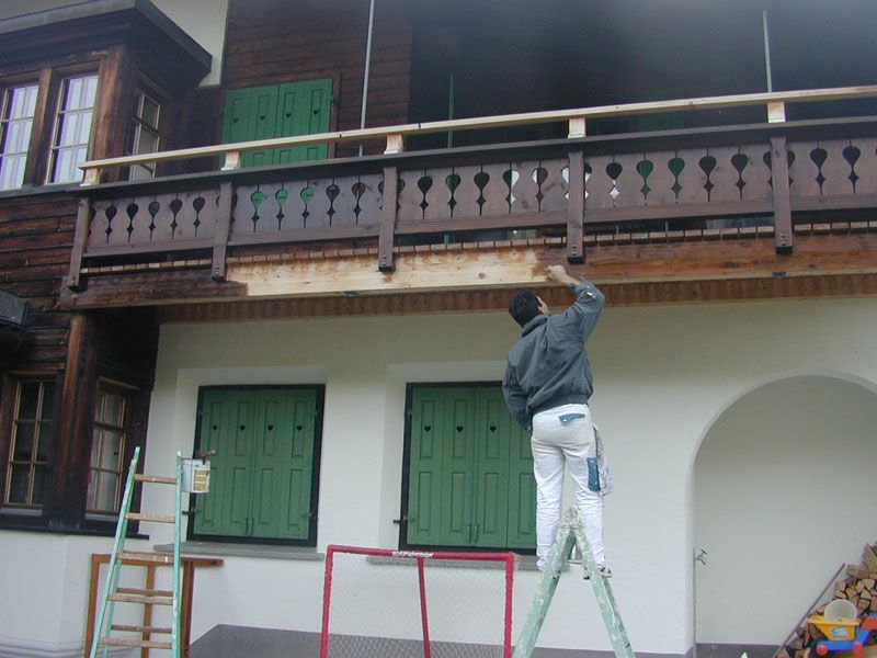 Maler streicht die Fassade unter einem Holzbalkon
