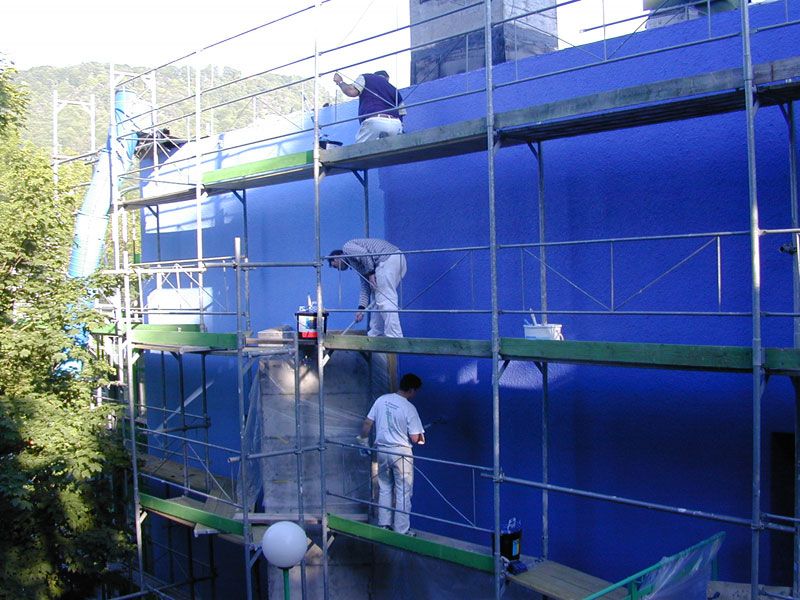 Maler auf dem Gerüst vor einer kräftig blau gestrichenen Fassade