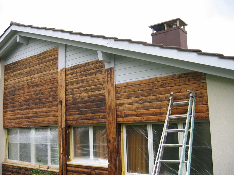 Holzfassade eines Wohnhauses während der Behandlung, eine Leiter lehnt an der Wand