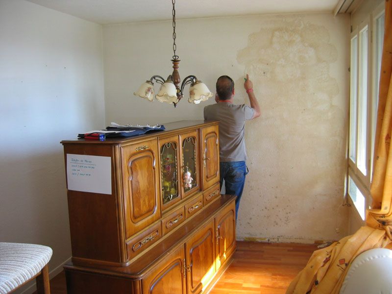 Maler bessert eine fleckige Wand in einem Wohnzimmer aus